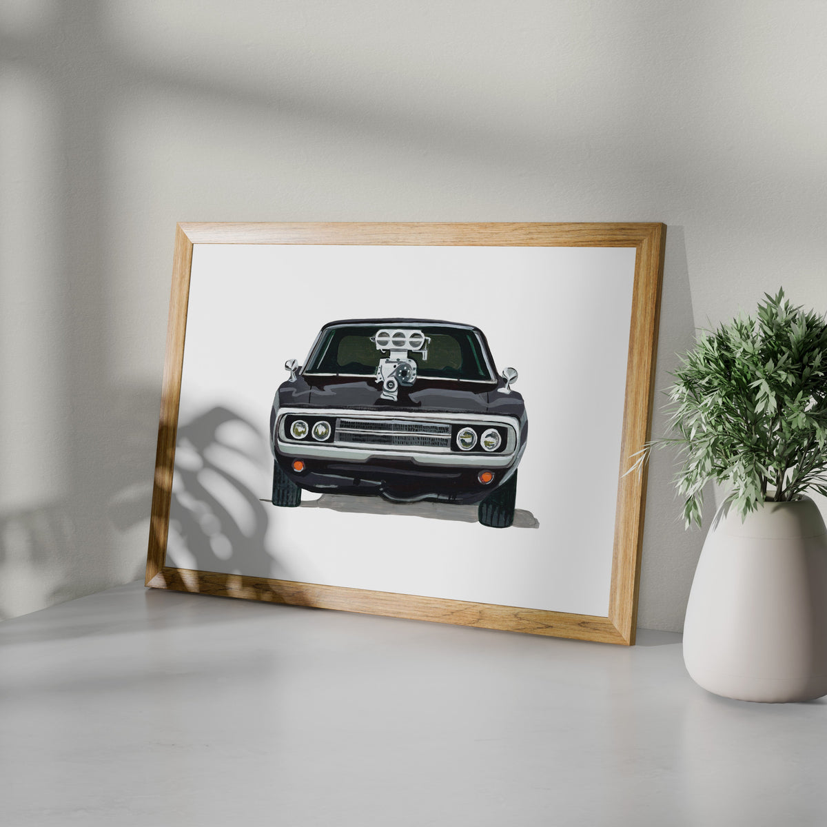 Black Dodge Charger R/T art print in a wooden frame beside a potted plant