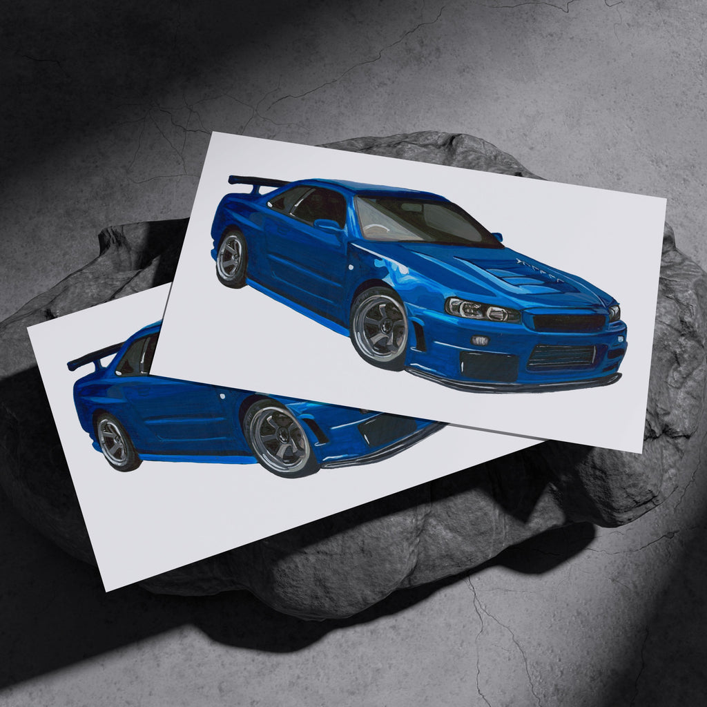 Two blue Nissan Skyline GT-R R34 art prints resting on a dark stone surface
