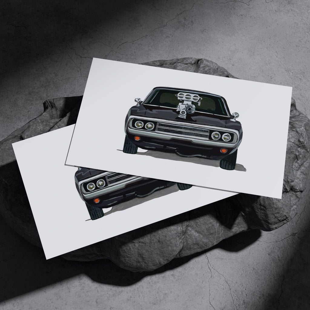 Two black Dodge Charger R/T art prints resting on a dark stone surface
