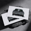 Two black Dodge Charger R/T art prints resting on a dark stone surface