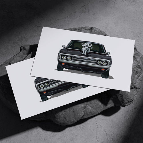 Two black Dodge Charger R/T art prints resting on a dark stone surface