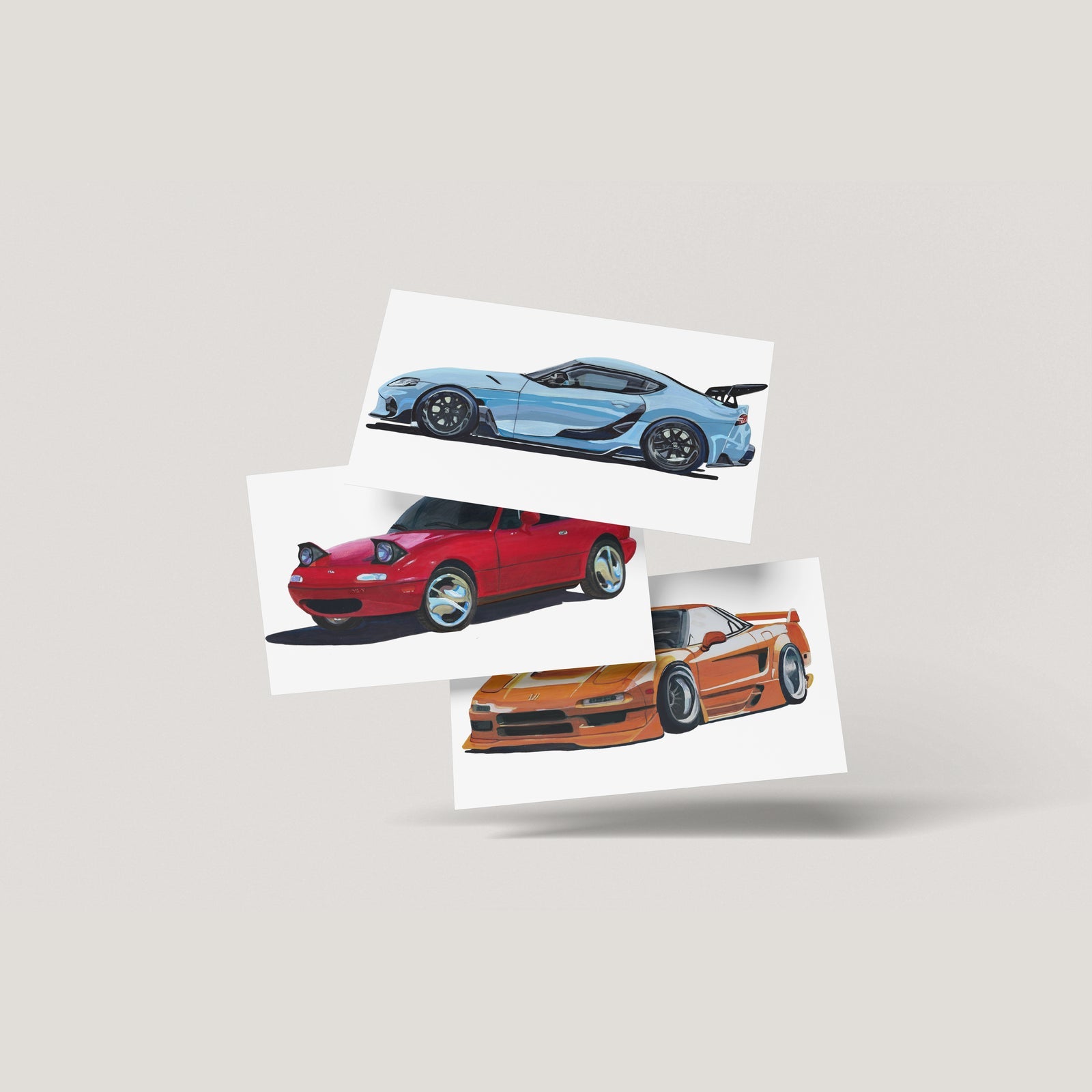 Three car art prints in light blue, red and orange fanned out on an off-white background