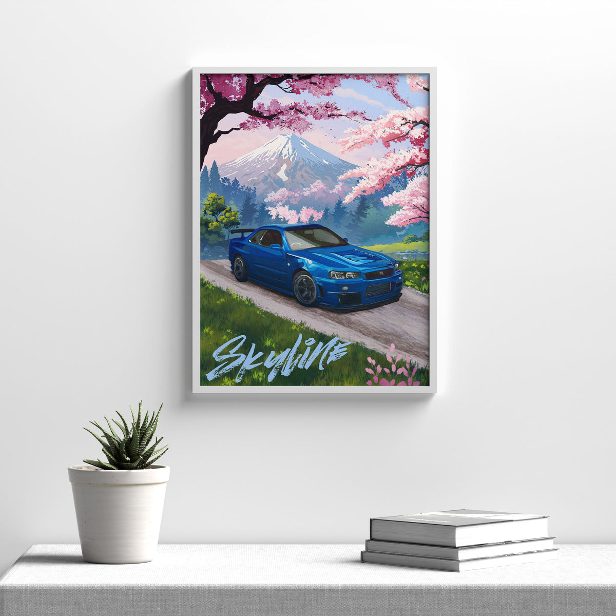 Blue Nissan Skyline GT-R R34 art print in a white frame hanging above a console table with a small plant and books