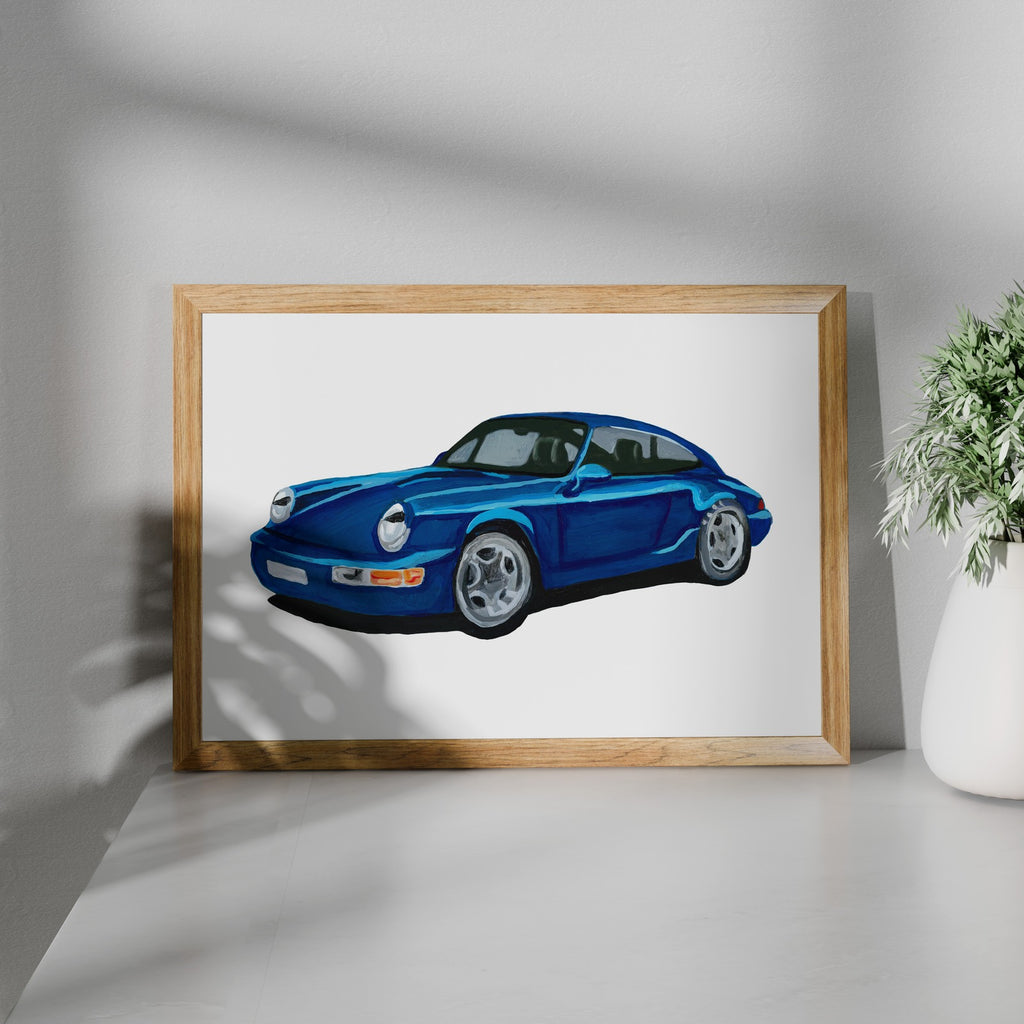 Blue classic sports car art print in a wooden frame beside a potted plant