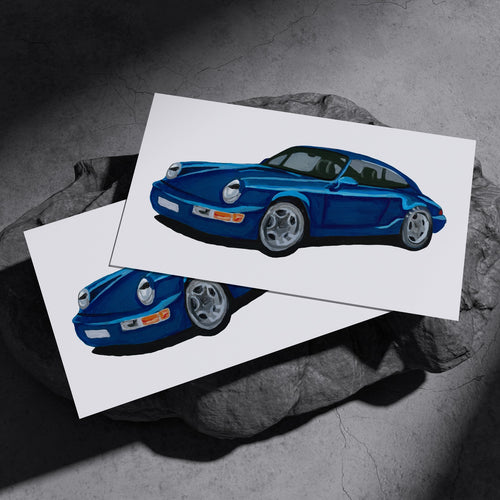 Two blue Porsche 964 Carrera RS art prints resting on a dark stone surface