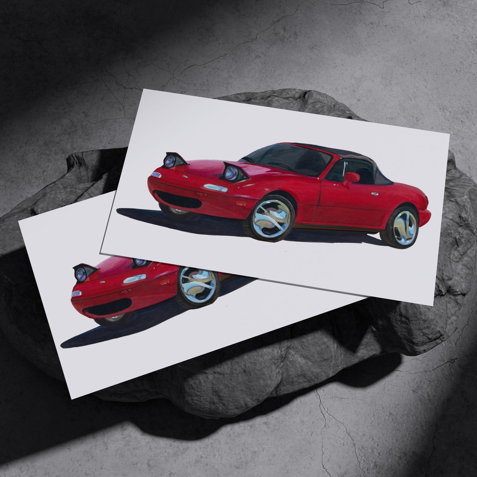 Two red sports car art prints resting on a dark stone surface