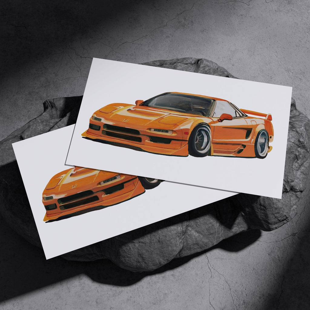 Two orange sports car art prints resting on a dark stone surface