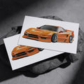 Two orange sports car art prints resting on a dark stone surface