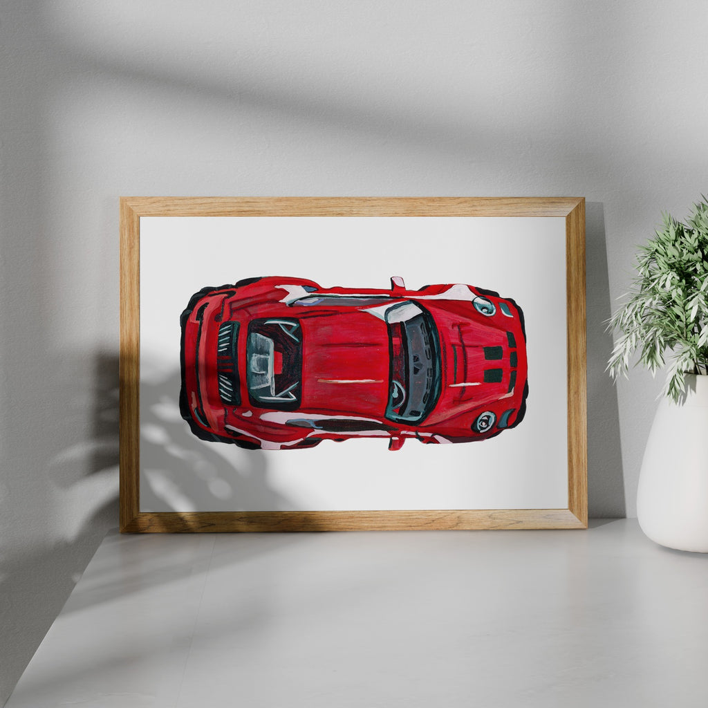 Red sports car art print in a wooden frame beside a potted plant