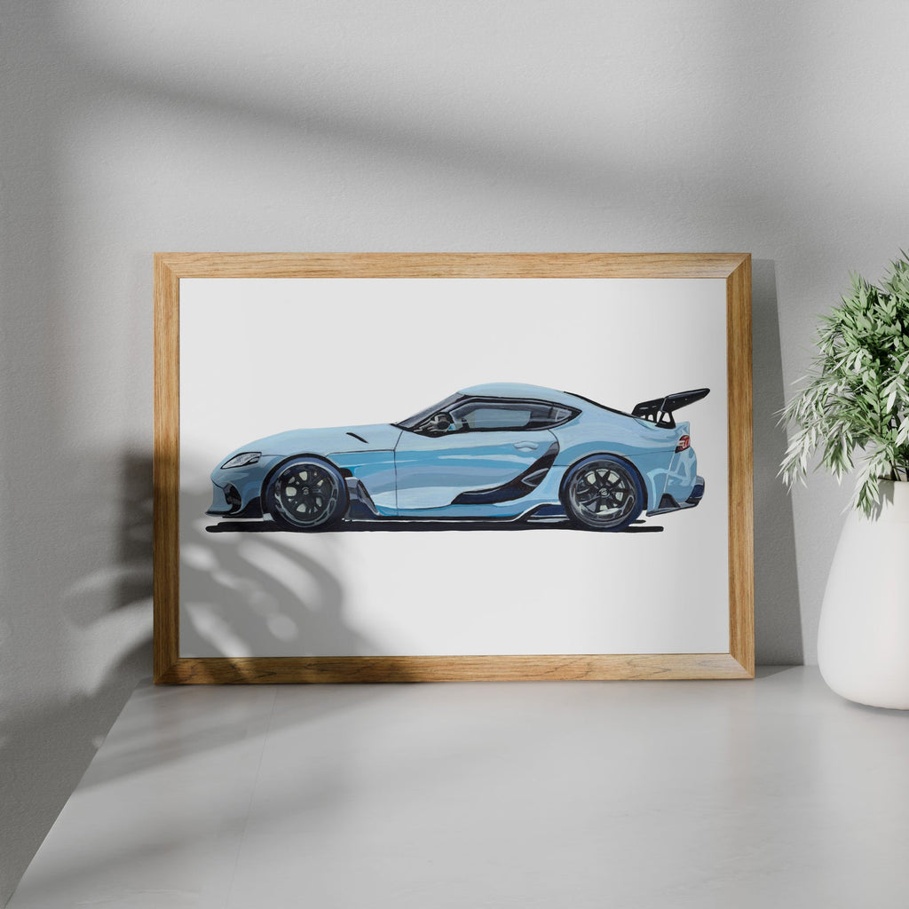 Light blue sports car art print in a wooden frame beside a potted plant