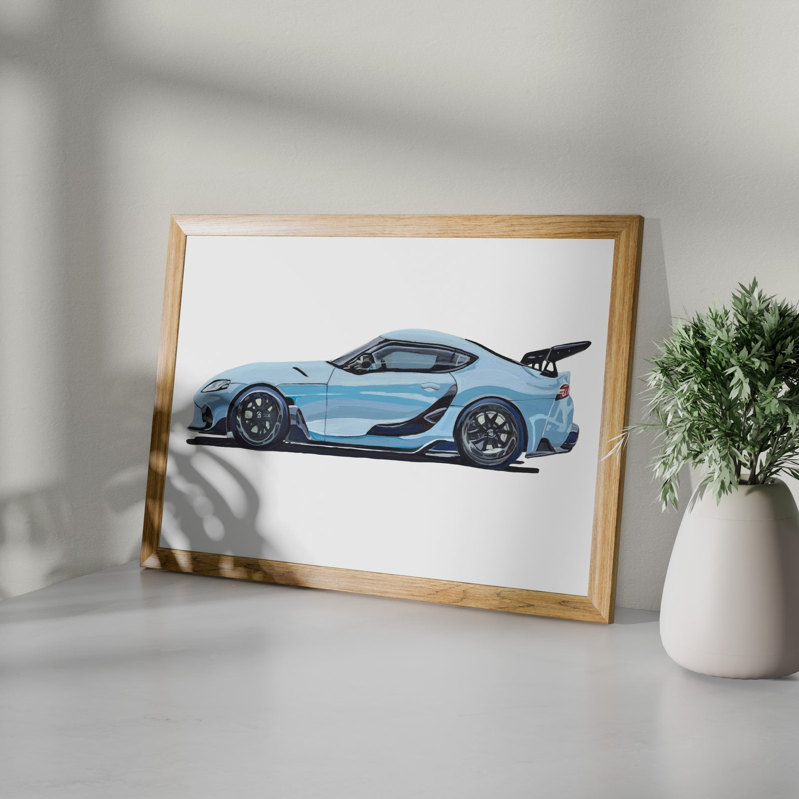Framed light blue sports car art print shown at an angle on a white surface