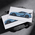 Two light blue sports car art prints resting on a dark stone surface